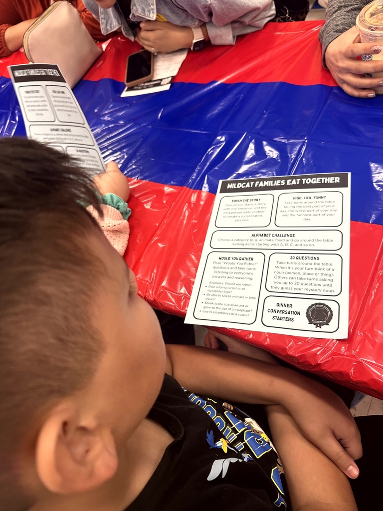 A student looks at a handout titled Wildcat Families Eat Together which features various dinner conversation starters.