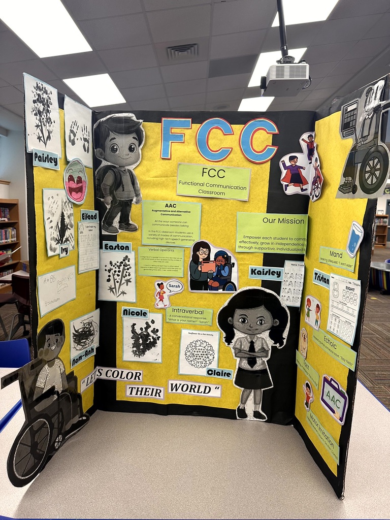 A yellow and black display board for the Functional Communication Classroom featuring student work and the mission statement.