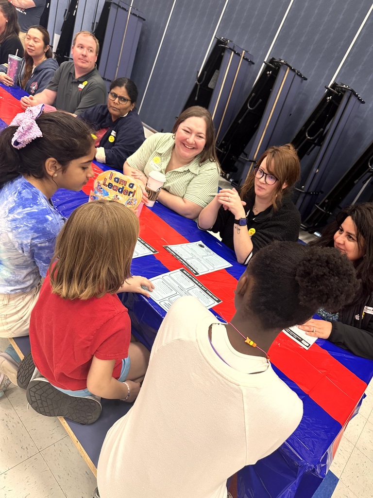 Parents and students sit together at a cafeteria table engaging in conversation during a leadership activity.