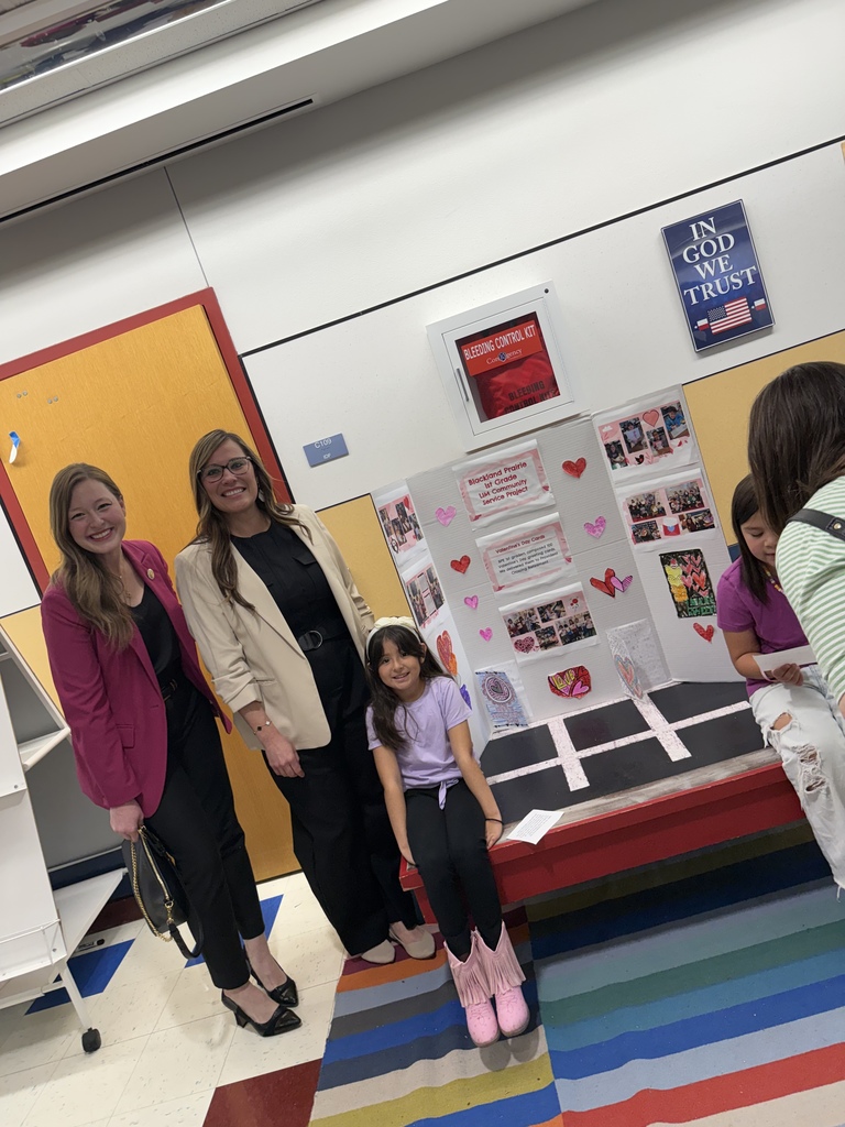 Representative Caroline Harris Davila and Ms. Borunda stand with a first grade student in front of a Blackland Prairie Community Service Project display board featuring student work.