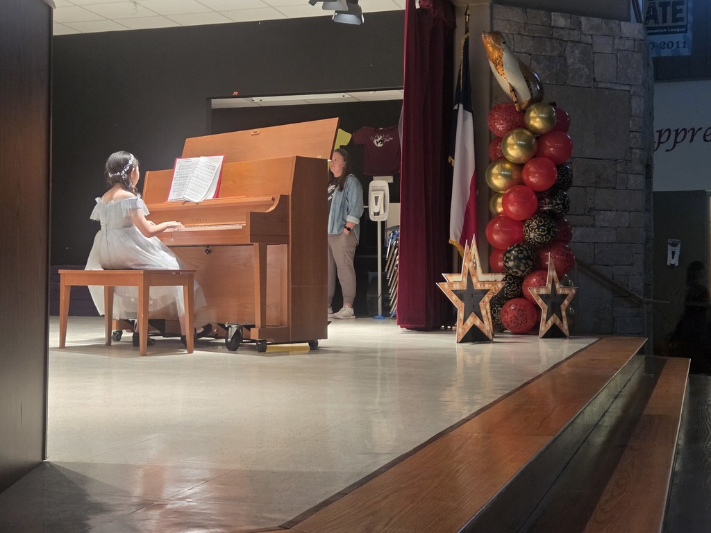 Photograph of student playing the piano on stage next to a balloon arch and stars