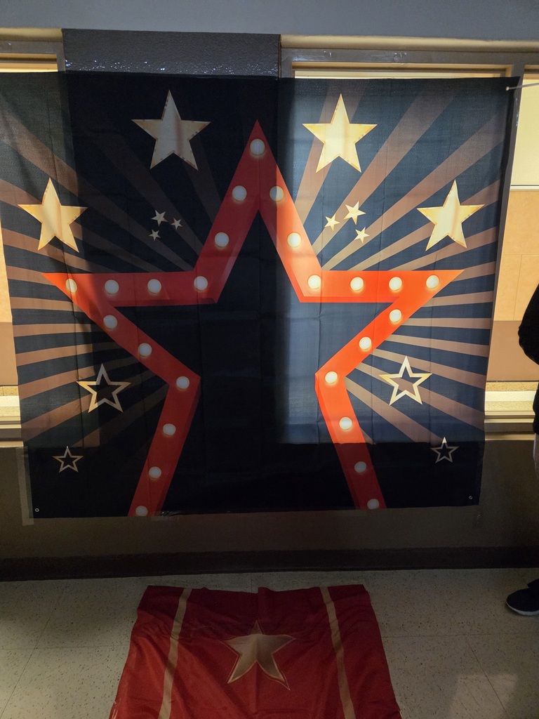Phtograph of a navy blue backdrop with a red star outline with small white stars and beams around it