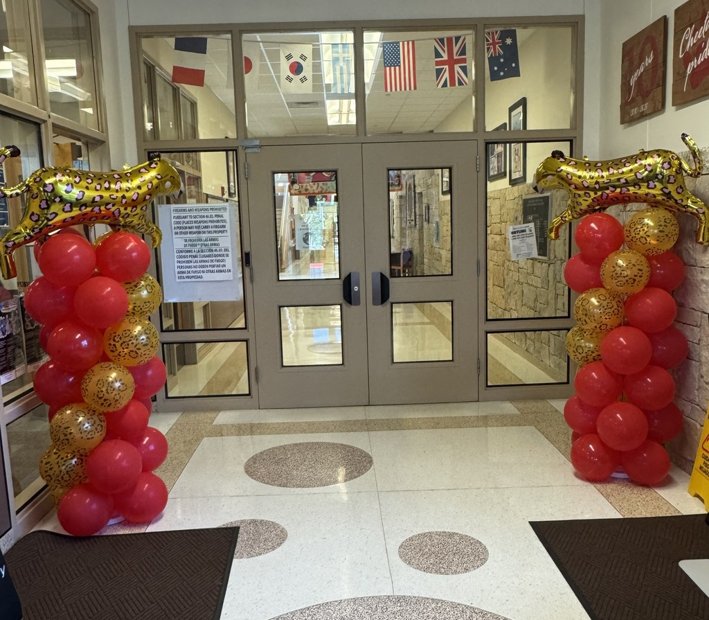 Photograph of two balloon towers with red and gold balloons and Cheetah Balooon on top on either side of a double set of doors and windows
