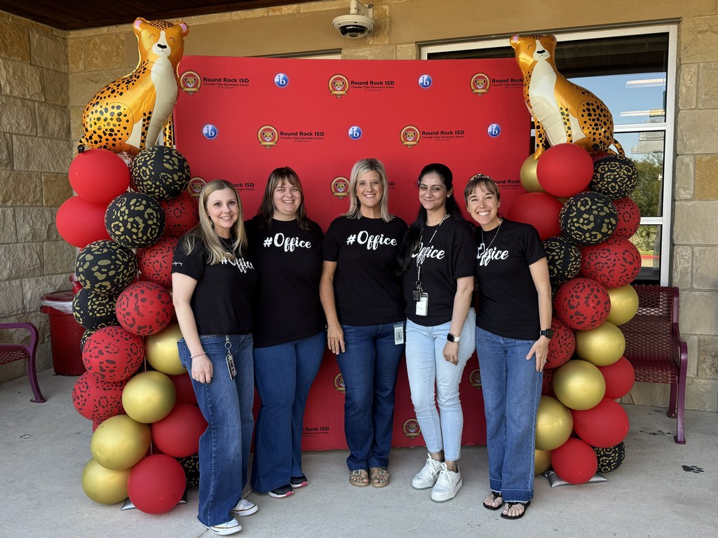 Photograph of the five office staff ladies standing in front of red backdrop with teh Chandler Oaks Logo and IB log on it with the words Round Rock ISD Chandler Oaks Elementary School World IB School. There is a red, black, and gold balloon tower onboth sides of the backdrop with a Cheetah Balloon on top of each