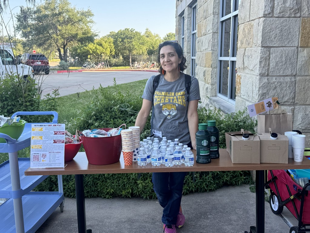 Photograph of PTA member standing behind a table outside with drinks, cups, waterbottles, and Coffee Containers