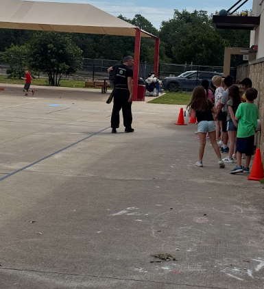 Students standing by the wall outside on the basketball courts and a martial arts instructor standing in front of them
