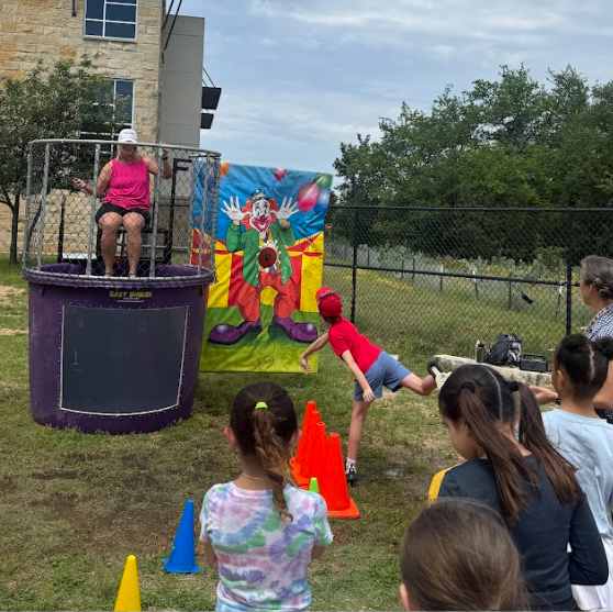 Students watching another student throw a ball and the principal sitting at the top of a dunk tank outside