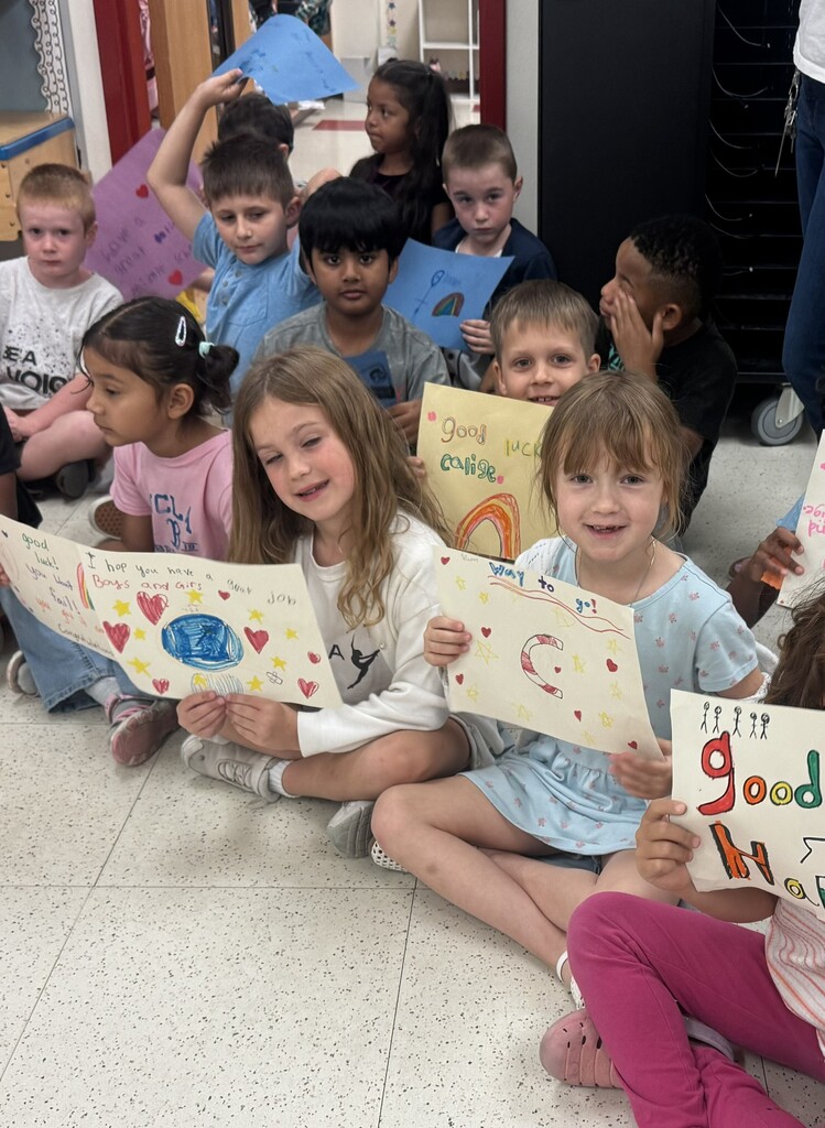 Students sitting on the floor holding signs they decorated to congratulate the seniors