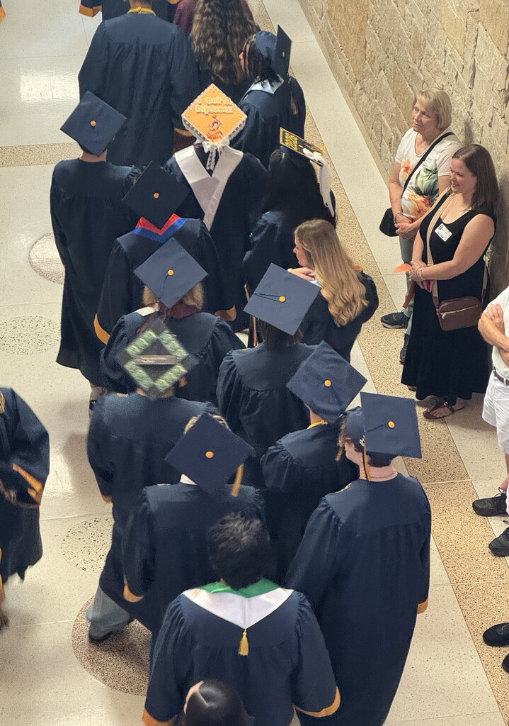 Photograph from overhead looking down at senior students dressed in Navy Blue Cap and Gowns walking down the hallway