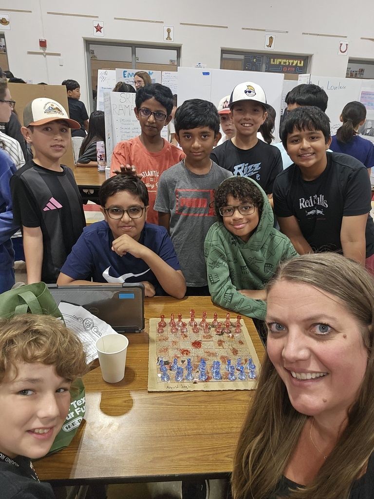 Principal playing chess with a group of students.