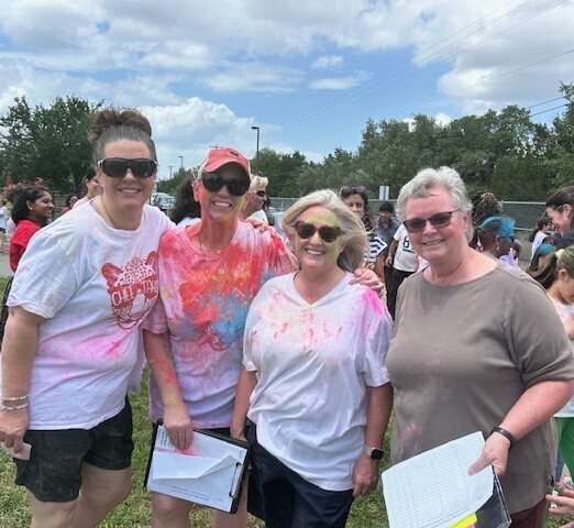 The 5th grade teachers standing outside holding papers and covered in different color dyes