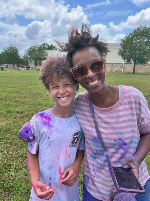 Student and adult covered in different colored dyes hugging for photo outside in front of grass