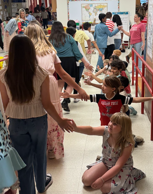 5th grade students walking through the hallway and younger students cheering them on and giving them a high five