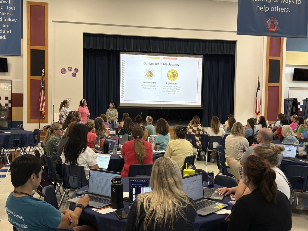 Blackland Prairie Elementary staff sitting at round tables with laptops during a Leader in Me training presentation in the cafeteria.