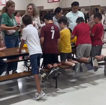 Five students kneeling on bench, building with legos at table. Two teachers and parent are facing them.