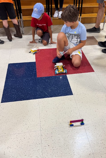 Two students kneeling on floor next to lego robot builds
