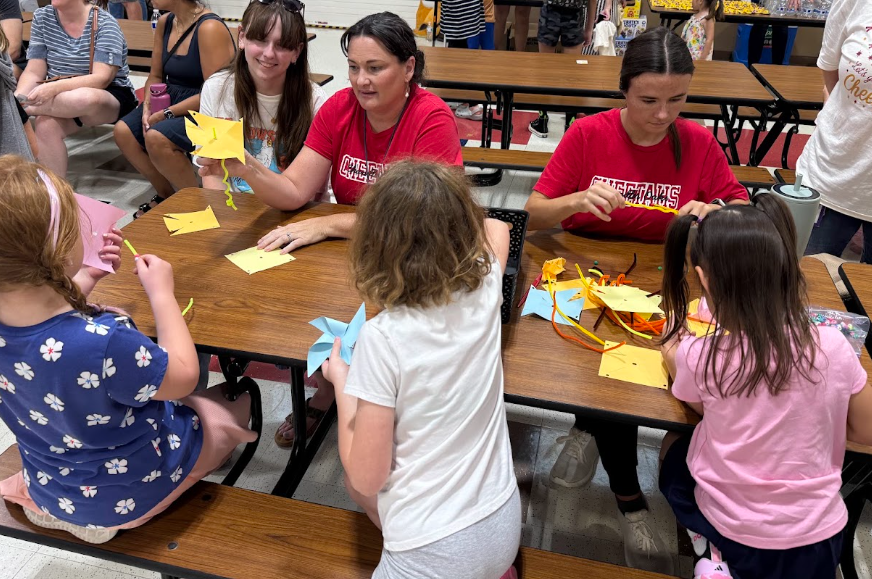 Three Adults sititng facing three students who are using paper to make pinwheels