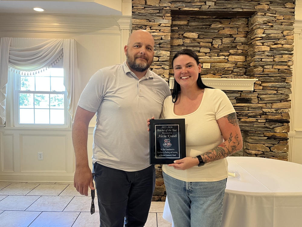Jeremy Martin (Left) and Alecia Knaub (right) smiling while Alecia holds a plaque for the 2025-2026 Teacher of the Year