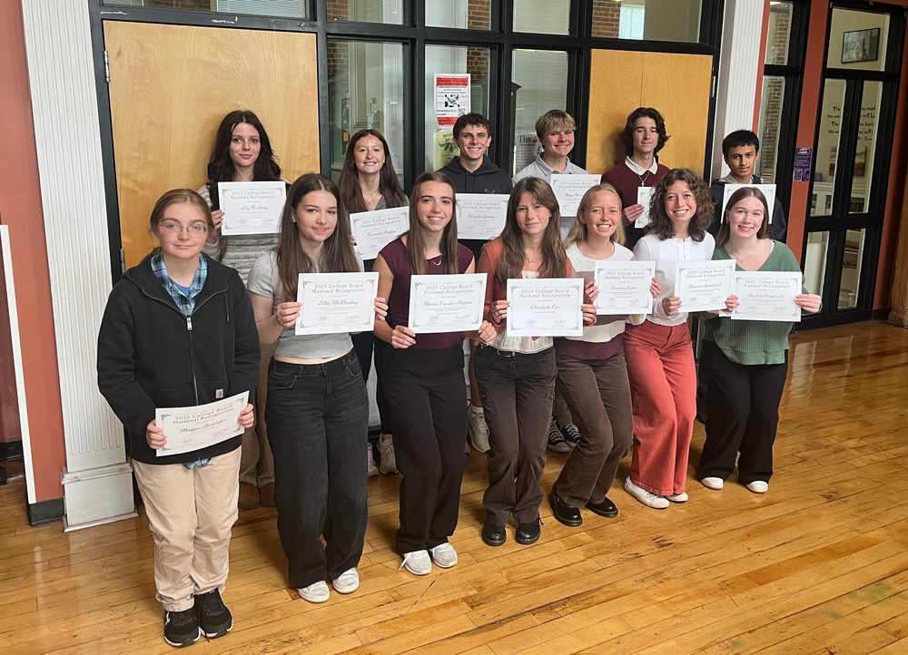 13 students pose in front of the RCS library holding certificates