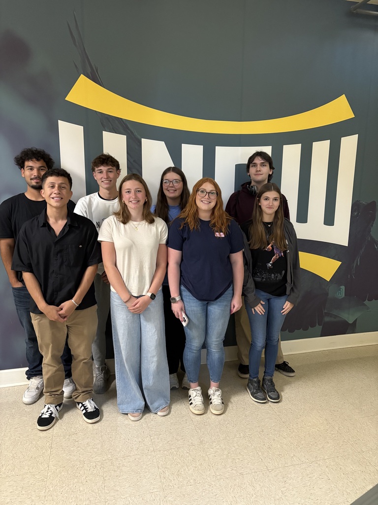 8 RCS seniors standing in front of a wall with UNC-W written on it.