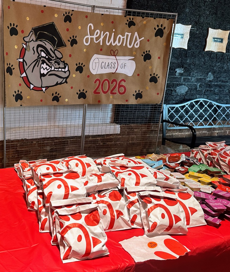 a table full of Chick-fil-A sandwiches with a red table cloths and a sign that say Class of 2026 behind it.