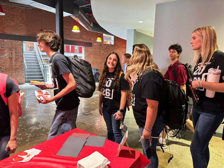 students stand in line, smiling to receive their lunch.