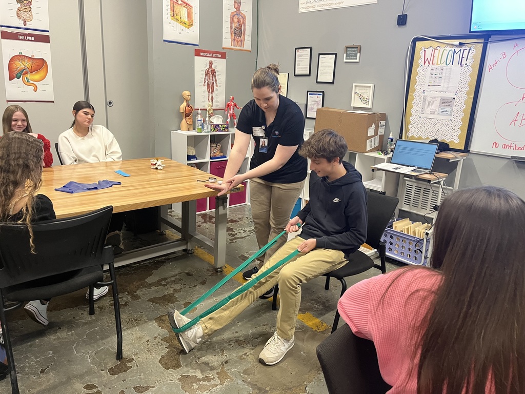Whitney showing a student how to stretch his leg with a green band. 