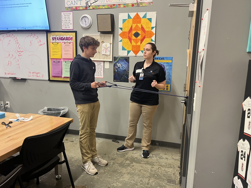 Whitney helping a male student use bands to stretch his arms and shoulders. 