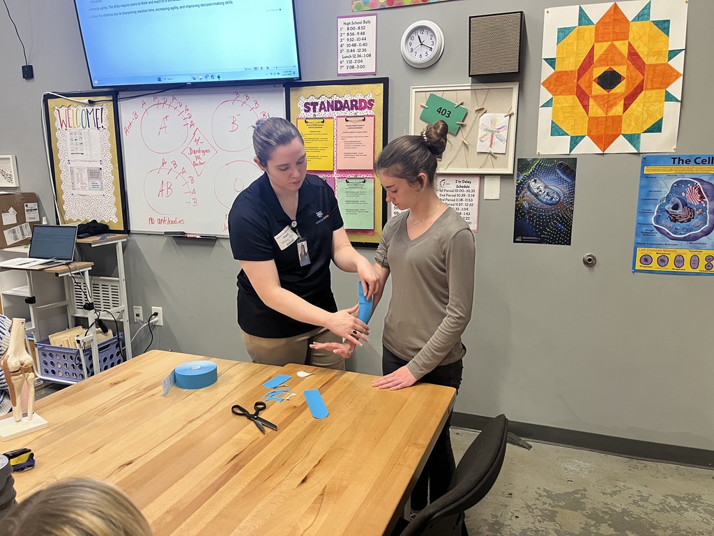 Whitney putting blue KT tape on a female student's arm. 