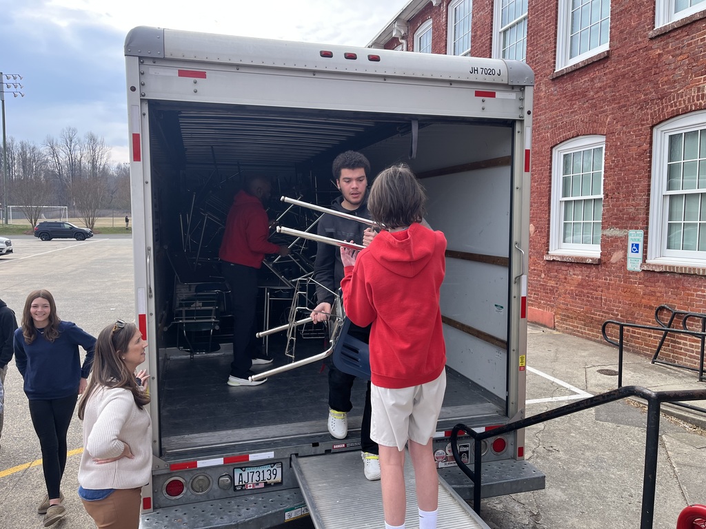 A student handing another student a desk from a truck full of desks