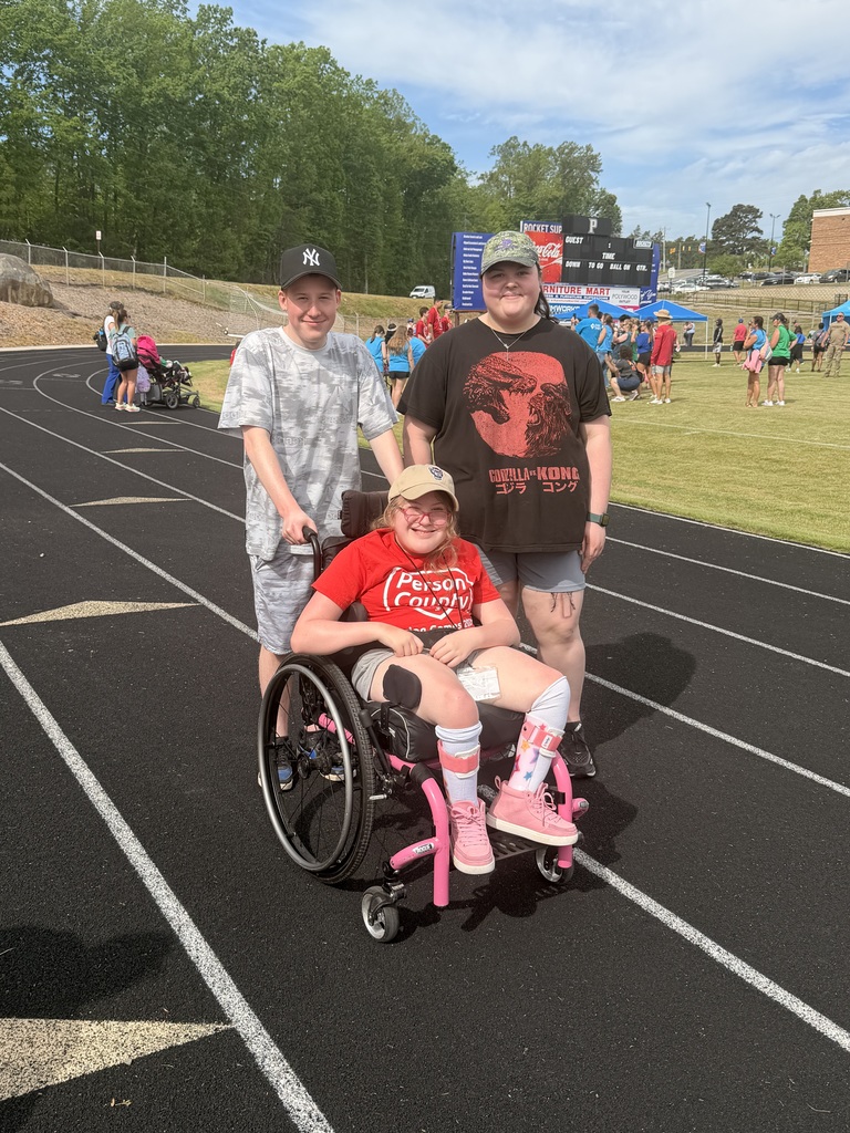 A young girl in a wheelchair smiling with a teen boy and a teen girl standing behind her. 