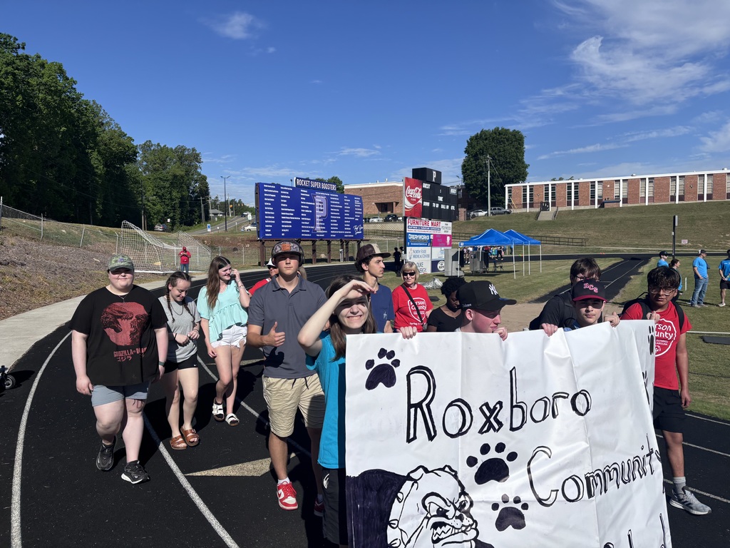 A group of students walking on a track outside, holding a sign that says Roxboro Community School