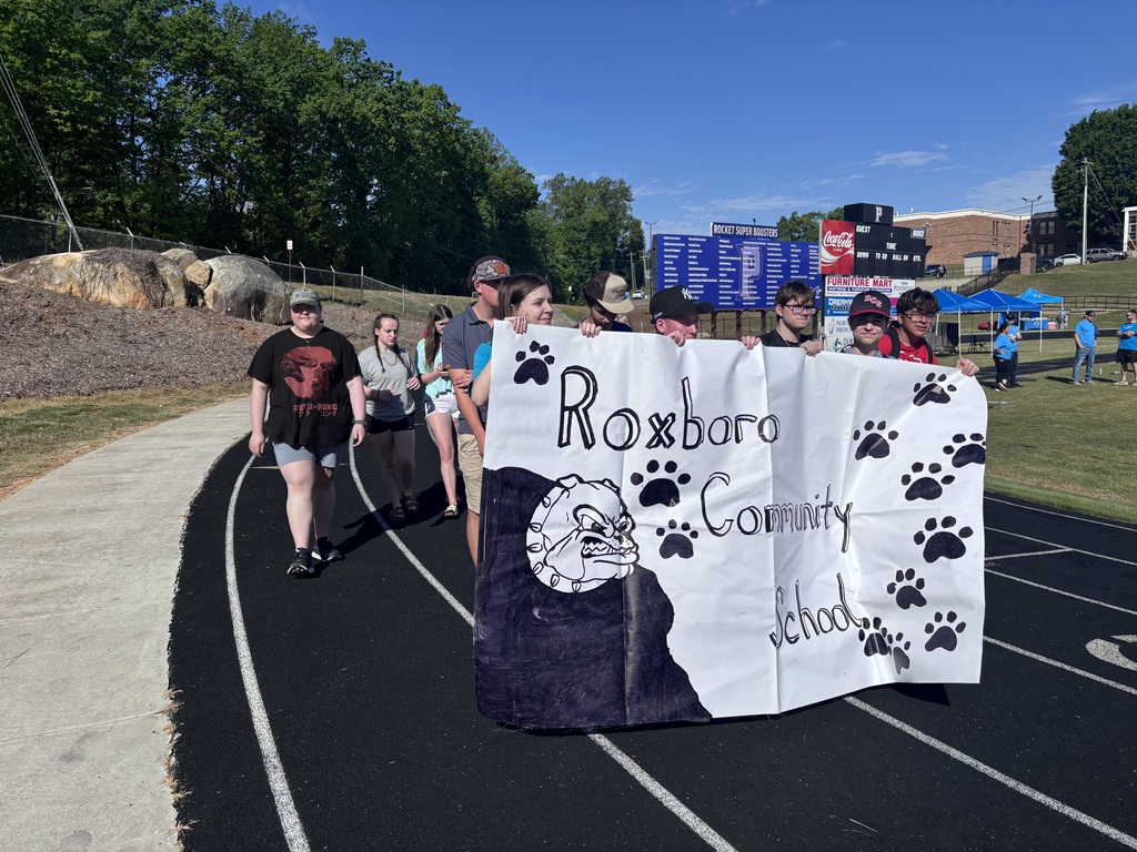 A group of students walking on a track outside, holding a sign that says Roxboro Community School.