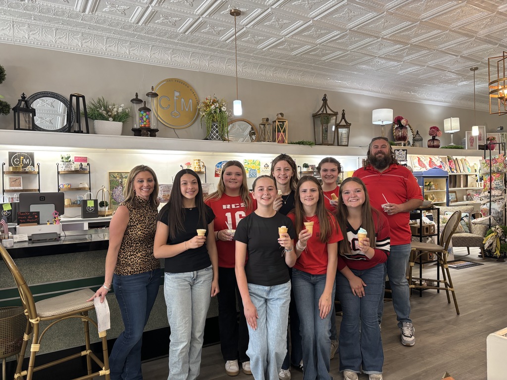 A group of 8 teenage girls holding ice cream cones with an adult woman on the left of them and a male teacher to the right of them