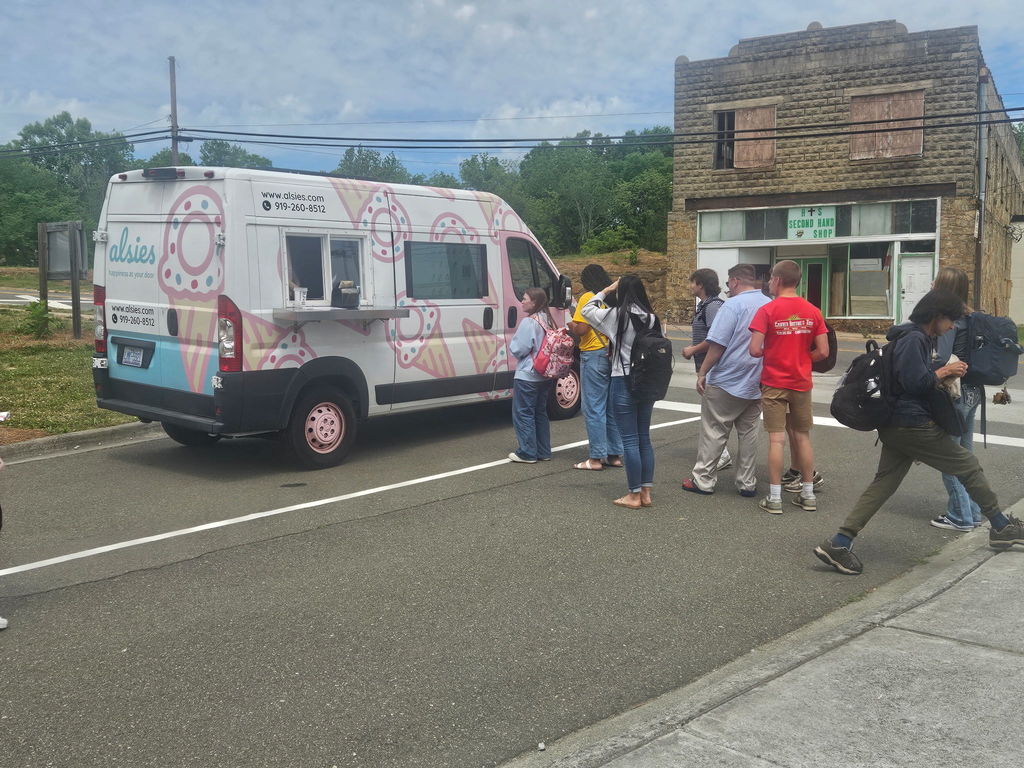 High school students standing in line for the ice cream van in a parking lot. 