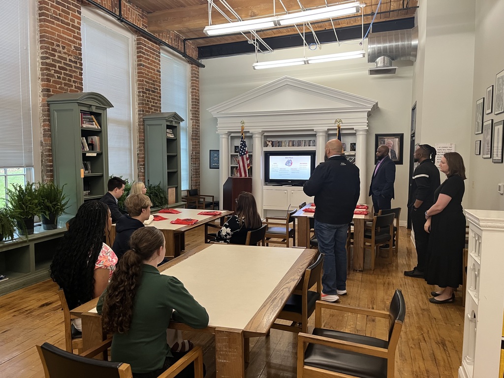 a group of people standing, presenting to a group of people sitting at tables