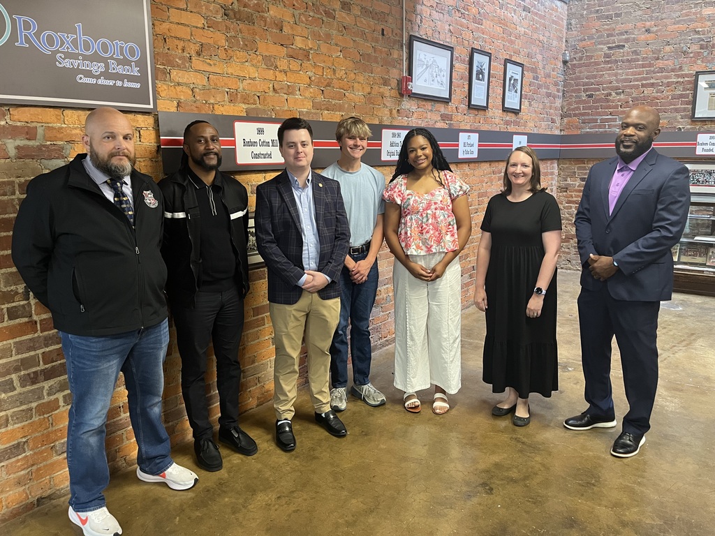 A group of 7 people smiling, standing in front of a brick wall at RCS