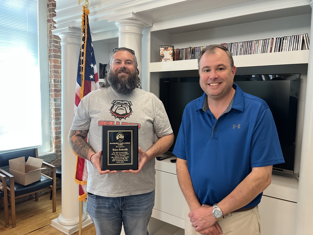 From left to right, Nelson Baskerville and Kyle Puryear smiling in the RCS library. Nelson is holding a plaque.