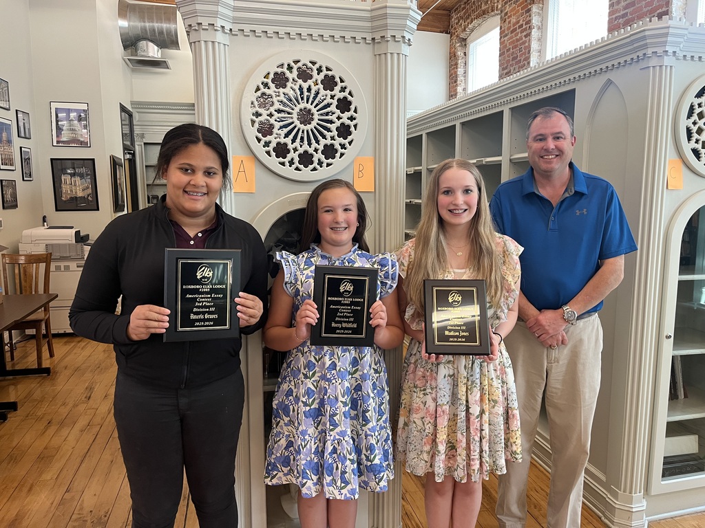 From left to right, Ameris Graves, Avery Whitfield, Madison Jones, and Kyle Puryear standing in the RCS Library. The girls are all holding plaques. 