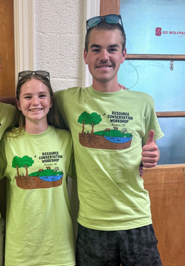 Kaitlin Carver and Sam Carver smiling in green tshirts that say "resource conservation workshop" and Sam is giving a thumbs up. 