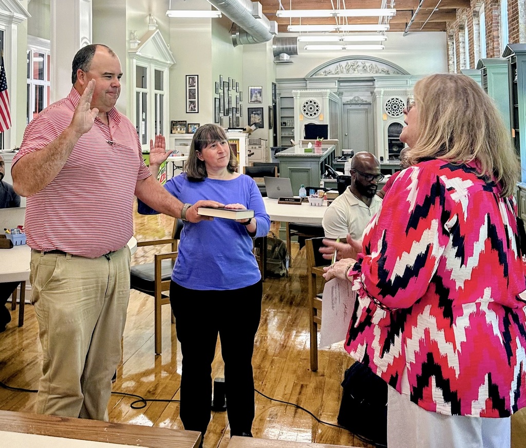 Left to right, Garrett Whitfield and Christy Grissom with their left hands on a bible, holding up their right hands, taking the oath of office with Deborah Barker to the right of them reading the oath. 