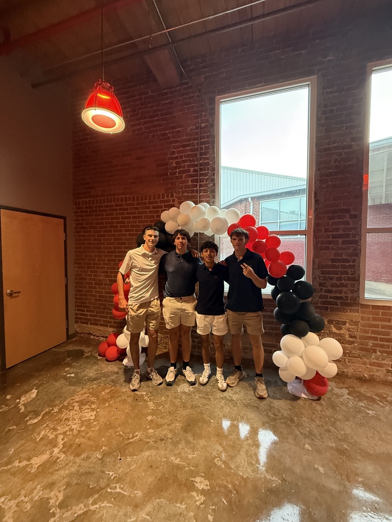 4 teenage boys smiling, standing in front of a balloon arch