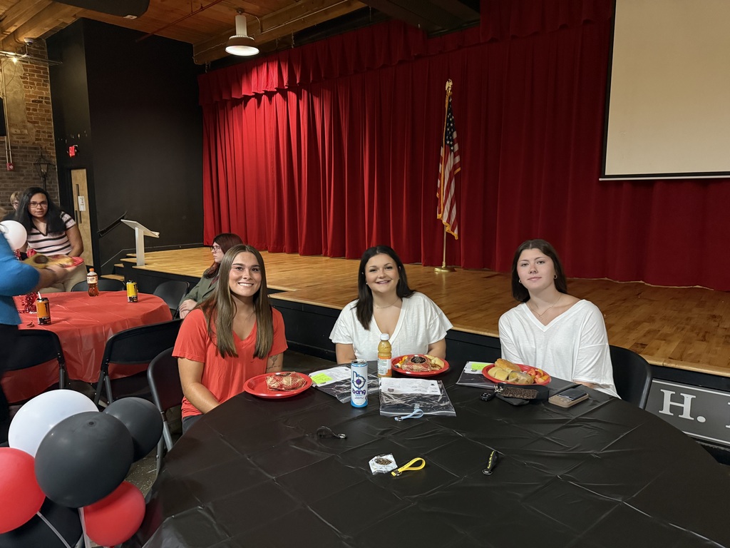 3 teenage girls sitting at a table with a black table cloth and plates of food