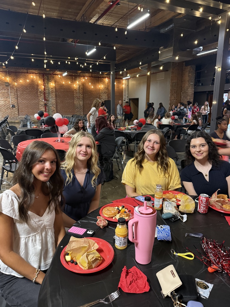 4 teenage girls smiling, sitting at a table with a black table cloth and plates