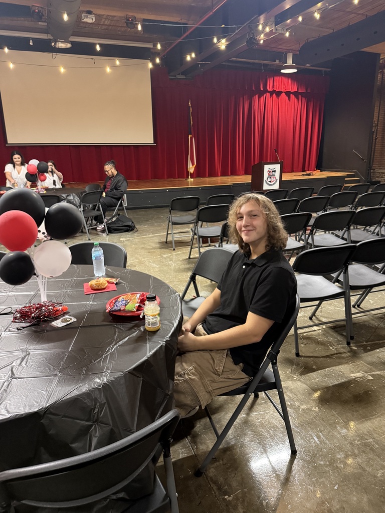 A teenage boy sitting at a table with a black tablecloth with a plate of food