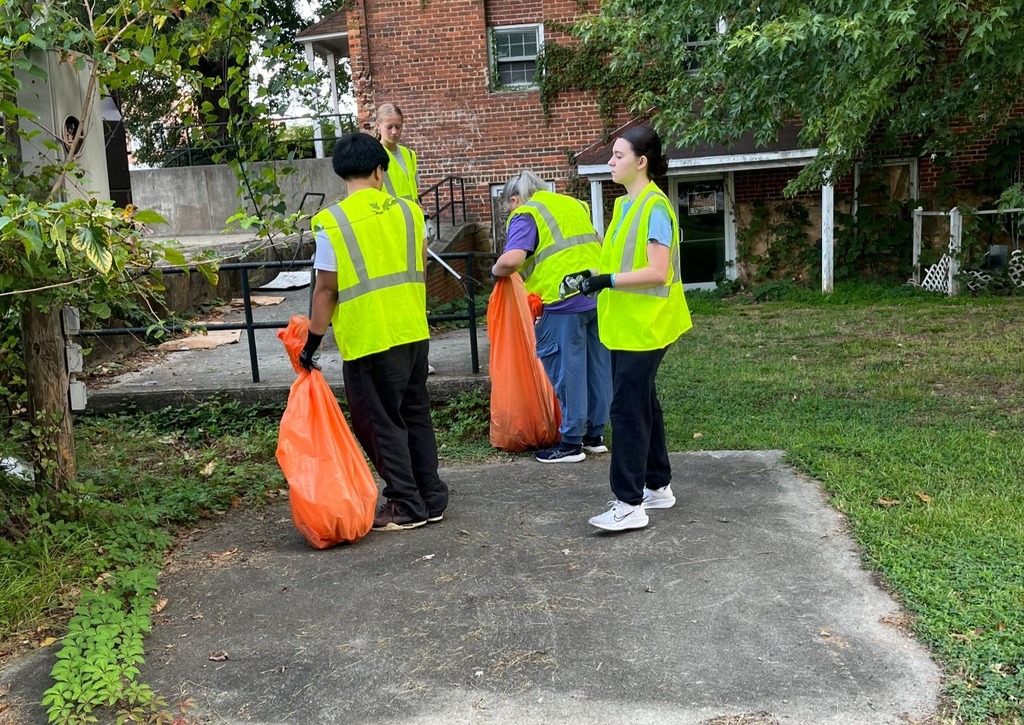 4 people in yellow safety vests picking up trash behind a business.