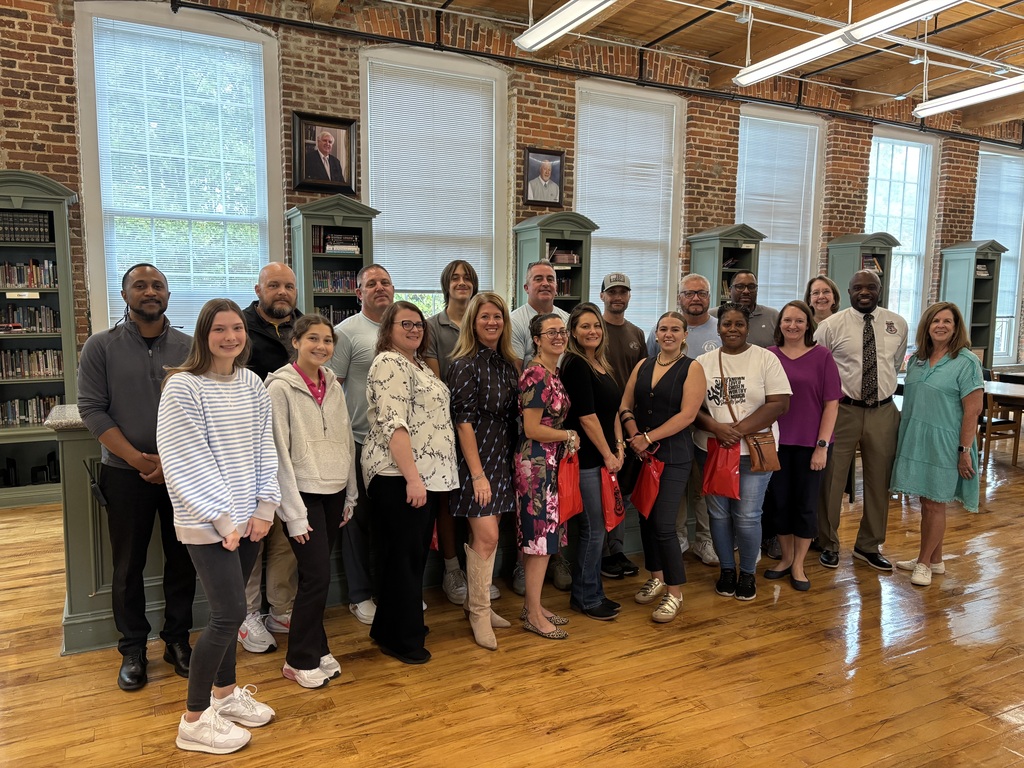 A group of adults and a few middle school students standing in the RCS library, smiling for a photo.