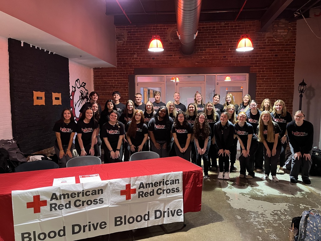 A group of teenage students posing in front of a table for an American Red Cross Blood Drive. 