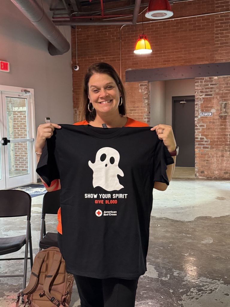 A female holding a black tshirt with a white chost on it that says "Show Your Spirit, Give Blood" on it.