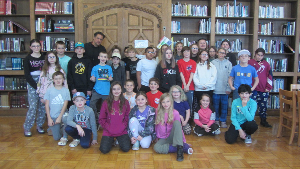 Pablo Cartaya posing for a picture with elementary students in a library 